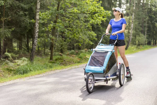 Młody dopasowanie matka kobiety w line Skating na świeżym powietrzu z Baby spacer — Zdjęcie stockowe