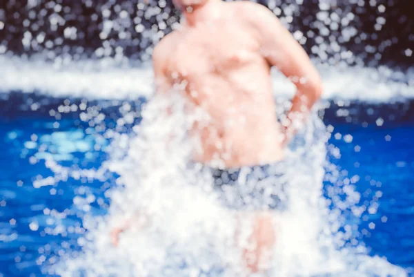 Knappe gespierde jongen springen uit het water wazig de achtergrond bokeh — Stockfoto