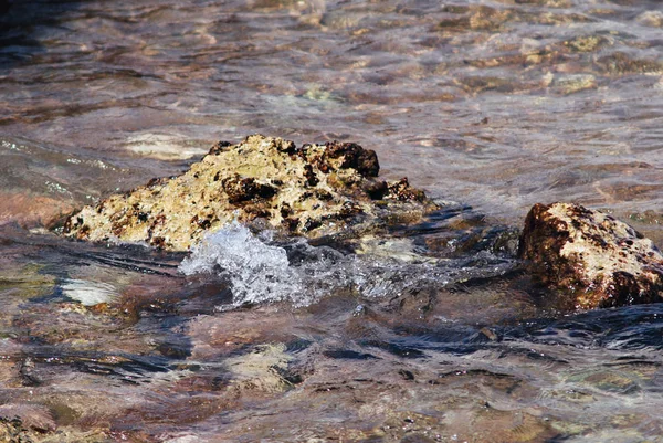 Фото красивої чистої бірюзової поверхні морської води з бризами і яскравими бризками на морському фоні, що вражають скелі — стокове фото