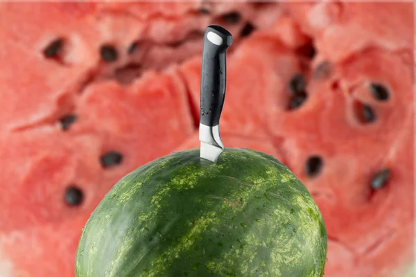 Созревший арбуз с ножом и красным мясным фоном — стоковое фото