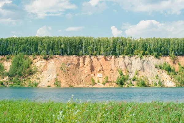 Lago azul con las colinas de arena amarilla naranja montaña y bosque en la parte superior contra el cielo — Foto de Stock