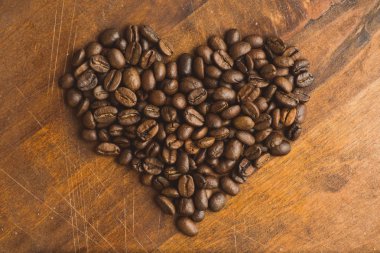Kalp, closeup makro kahve çekirdekleri için arka plan ve doku şeklinde kahverengi kahve çekirdekleri. Kahverengi ahşap tahta üzerinde.