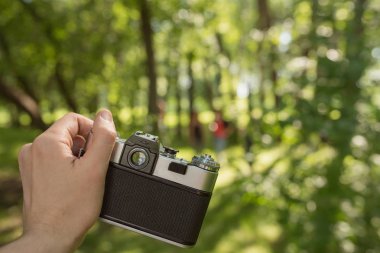 Retro eski film kamera parlak güneşli yeşil orman üzerinde tutan adam el bokeh arka plan bulanık. POV görünümü