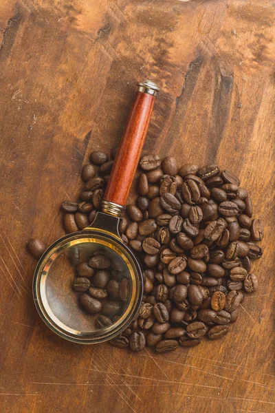 Brown coffee beans in circle shape, closeup of macro coffee beans for background and texture. On brown wooden board with magnify glass. Copyspace — Stock Photo, Image