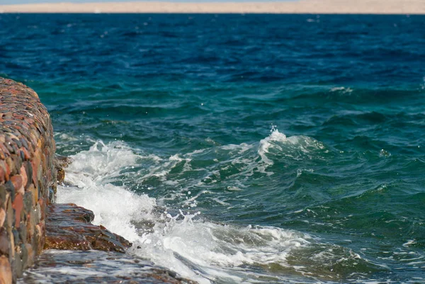 Photo of beautiful clear turquoise sea ocean water surface with ripples and bright splash on stone sea cape background, zdjęcie poziome — Zdjęcie stockowe