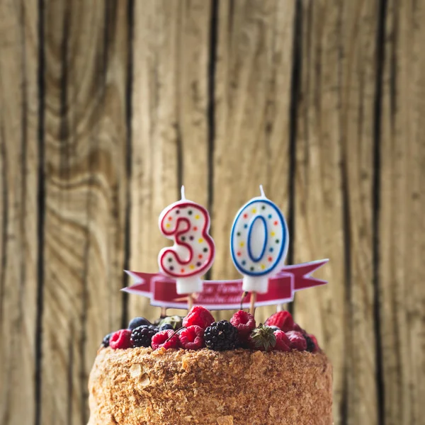 raspberries blackberry birthday cake with candles number 30 on wood background and copyspace for your text