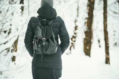 karlı orman ahşap .landscape planda deri sırt çantası ile siyah kış ceket giymiş bir güzel youngwoman arka fotoğrafını yürür