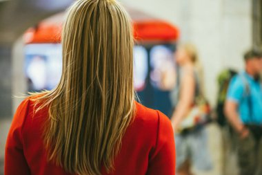 Arka omuz görünümü bir yeraltı tren ve yürüyen insanlar bulanık arka planı Kırmızı elbiseli güzel genç kızın üzerinde. Seçici odak ile sığ Dof vurdu. Seçim tereddüt