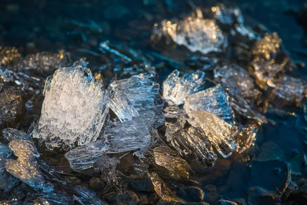 Pieces of melting ice under the bright Spring sun on the river bank. Selective focus macro shot with shallow DOF