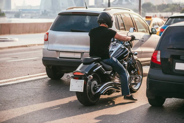 Achteraanzicht van een knappe biker gekleed in een zwart T-shirt en zwarte helm jeans en sneakers. Hij is rijden op de motorfiets van de kruiser op achtergrond van 2 auto's. Verkeerseinde — Stockfoto