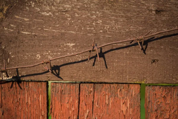 Ein Stück alter, lackierter brauner Zaun, auf dem rostiger Stacheldraht liegt. helles Sonnenlicht lässt Objekte kontrastreiche Schatten werfen — Stockfoto