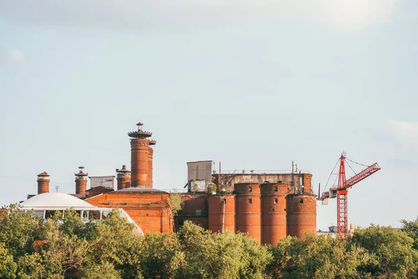 Old brick Factory on the background of the tops of the forest, with a construction crane aside