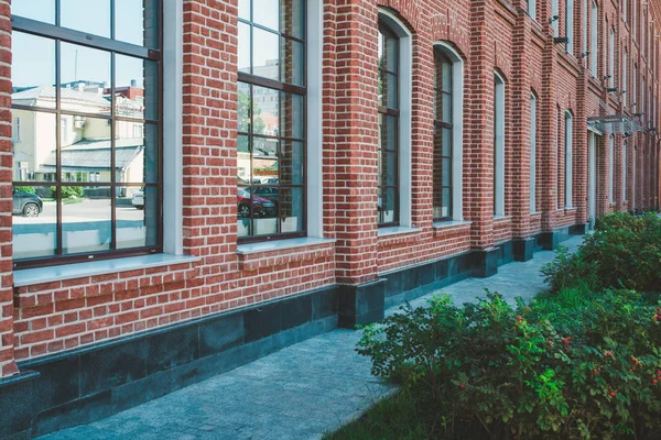 Office building in loft style. Large Windows. Red brick wall. Green bushes on the right. Perspective shot composition