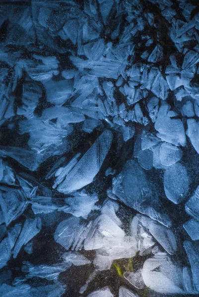 Réseau de fissures dans une épaisse couche de glace solide gelée avec de la lumière brillante et de l'herbe verte dans les profondeurs — Photo