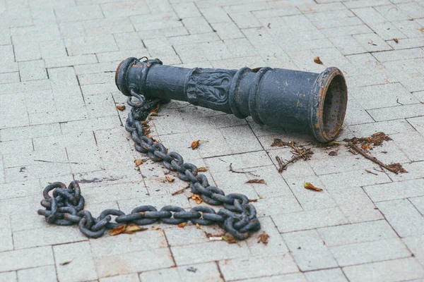 En gammal antik rostig baluster i metall med en tung kedja som ligger på en kakel i en park — Stockfoto