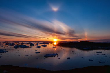 Sunset over Disko Bay in Greenland with circular halo effect. Halo is the name for a family of optical phenomena produced by sunlight interacting with ice crystals suspended in the atmosphere clipart