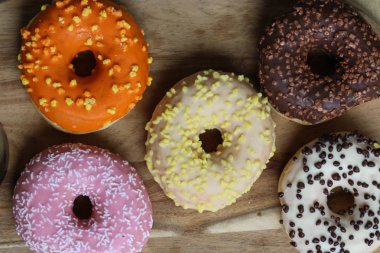 Ahşap arka planda farklı renkli çörekler. Çilekli, muzlu, çikolatalı, vanilyalı aromalı çörekler. Çörekler farklı süslemelerle süslenmiş..