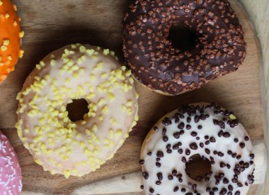 Ahşap arka planda farklı renkli çörekler. Çilekli, muzlu, çikolatalı, vanilyalı aromalı çörekler. Çörekler farklı süslemelerle süslenmiş..