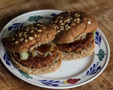 Ahşap arka planda tabakta taze vejetaryen soja hamburgerinin yakın görüntüsü. Hamburger soğan ve körili ketçap pişirdi.