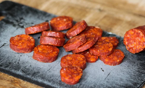 Embutidos de chorizo de cerdo español frescos hechos con pimentón, ajo, chile y romero, cortados en rodajas sobre una tabla de cortar negra — Foto de Stock