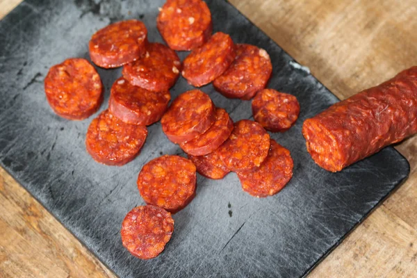 Embutidos de chorizo de cerdo español frescos hechos con pimentón, ajo, chile y romero, cortados en rodajas sobre una tabla de cortar negra —  Fotos de Stock