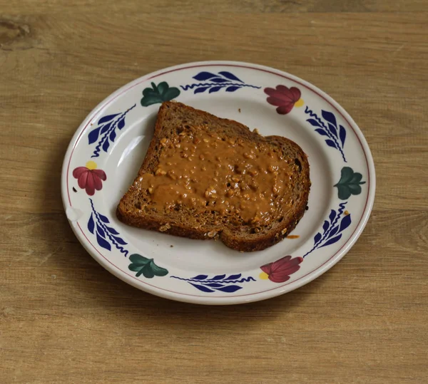 Brot mit Erdnussbutter auf weißem Teller auf Holzgrund — Stockfoto