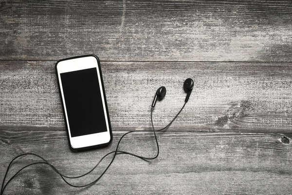 Mobile phone with earphone on wooden background