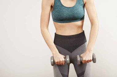 Sportif kadın gri arka planda Dambıl ile egzersizleri yapar.