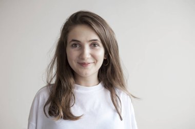 Genç güzel kadın gri arka planda kameraya bakıyor.