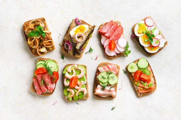 Set of different sandwiches with meat, vegetables, seafood. Assortment open sandwiches on light stone background. Tasty healthy snack. Top view, flat lay. — Stock Image Set Different Sandwiches Meat Vegetables Seafood Assortment Open Sandwiches Light Royalty Free Stock Images