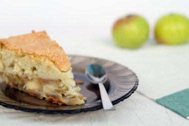 beyaz bir arka plan üzerinde kaşık ve meyve ile koyu bir cam tabak üzerinde elma kek parçası.