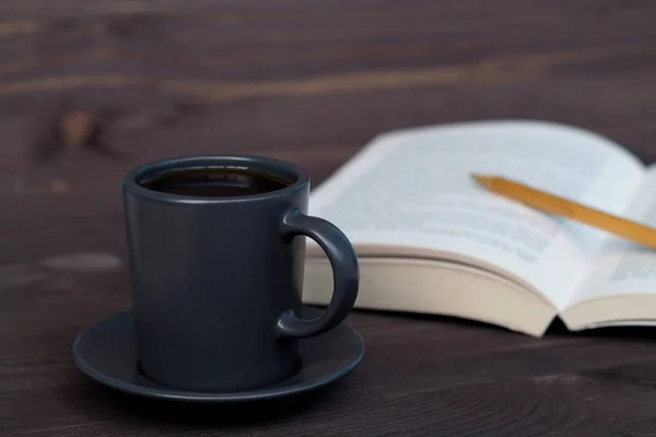 cup of coffee and book with pencil on the wooden table