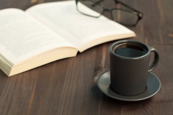 dark cup of coffee and book with glasses on wooden table