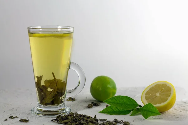 green tea with lemon and lime on the white table with green leaves