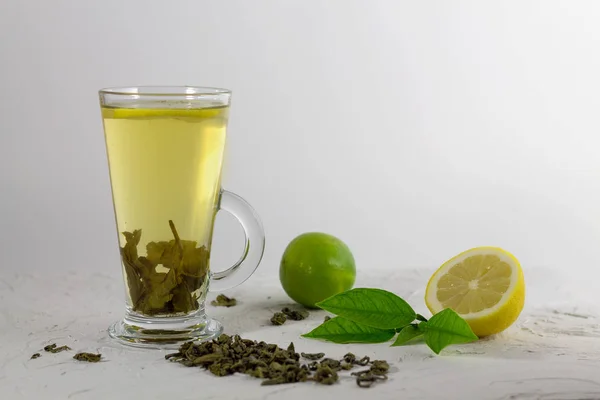 cup of green tea with lemon and lime on the white table with green leaves