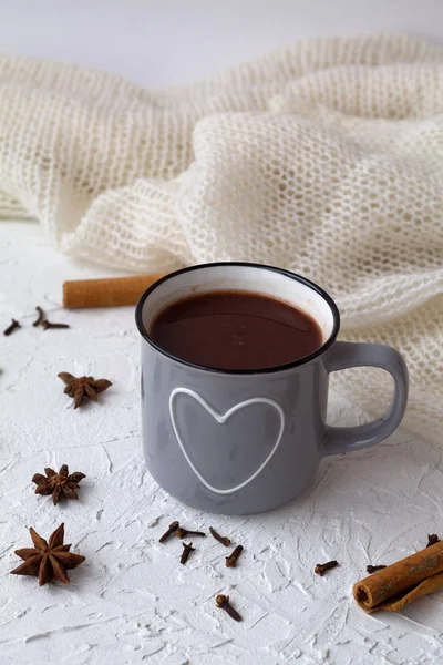winter and autumn hot drinks. cup of hot chocolate or cocoa and cinnamon, anise star with knitted white plaid on white background. copy space. vertical