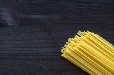 Makarna arka planında spagetti. Tahta masada spagetti. Siyah zemin üzerinde fotokopi alanı olan çiğ makarna. Üst Manzara. İtalyan Mutfağı.
