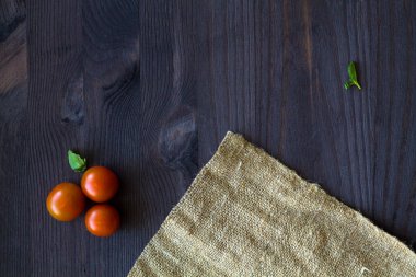 Kırmızı kiraz domatesleri ve yeşil yapraklar. Tahta bir masa üzerinde üzerinde, fotokopi alanı olan çuval bezi. en üstteki görünüm.