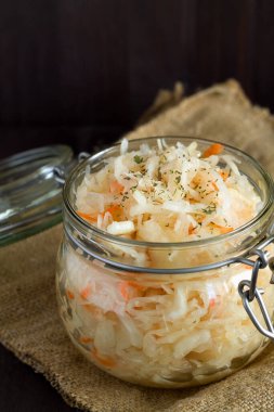 yakın plan ev yapımı lahana turşusu ve siyah arka planda cam kavanozda havuç ve otlar. Tahta masada çuval bezli lahana turşusu. Konserve yiyecek kavramı. kopyalama alanı. vejetaryen yemeği.