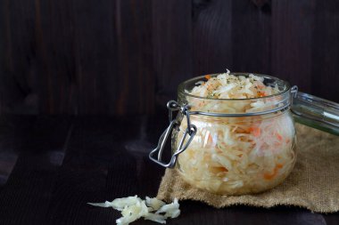 Ev yapımı lahana turşusu ve siyah bir arka planda cam kavanozda otlar. Ahşap masada çuval bezli lahana turşusu. kopyalama alanı. Konserve yiyecek kavramı. vejetaryen yemeği.