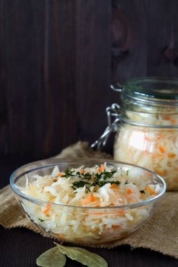 Ev yapımı lahana turşusu ve siyah arka planda cam tabakta otlar. Kavanozda lahana turşusu ve tahta masa örtüsü. Konserve yiyecek kavramı. kopyalama alanı. vejetaryen yemeği.