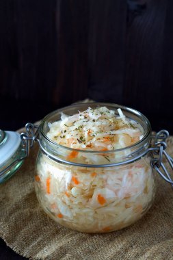 Ev yapımı lahana turşusu ve siyah arka planda cam kavanozda havuç ve bitkiler. Tahta masada çuval bezli lahana turşusu. kopyalama alanı. Dikey. Vejetaryen yemeği. Konserve yiyecek kavramı.