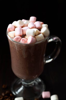 Marşmelovlu bir fincan kahve. Karanlık bir masada bir bardak kapuçino. Tahta arka planda sıcak çikolata. Sıcak içecekler kış ve sonbahar. Dikey. Boşluğu kopyala