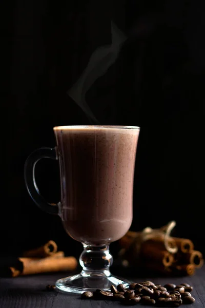 cup of cappuccino. hot drinks winter and autumn. glass of hot chocolate with coffee beans and cinnamon sticks on a dark background. hot drinks on a wooden background. vertical.copy space