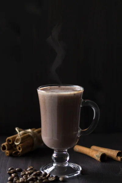 cup of cappuccino.hot drinks winter and autumn. glass of hot chocolate with whipped cream, coffee beans and cinnamon sticks on a dark background. hot drinks on a wooden background. vertical.copy space