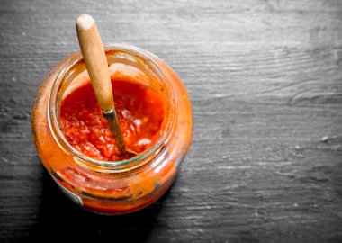 Bir cam kavanoza domates sosu. Siyah arka plan üzerine.