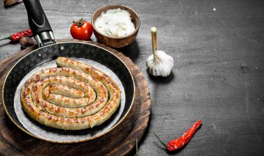 Sarımsak, domates ve otlar ile bir tavada kızarmış sosis. Siyah arka plan üzerine.