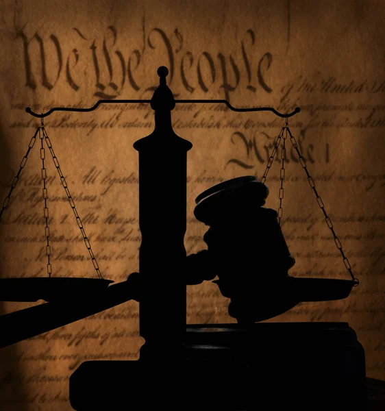 Court gavel and scales of justice silhouette over text of the US Constitution