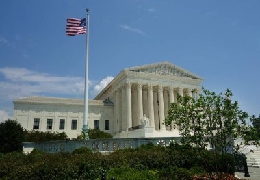 Washington DC 'deki Amerikan Yüksek Mahkemesi binasında mavi gökyüzünde dalgalanan Amerikan bayrağı                               