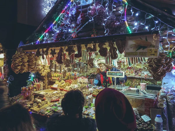 罗马尼亚布拉索夫 2018年12月2日 游客晚上在理事会广场的圣诞博览会上购买传统的椒盐卷饼 饼干和糖果 这些都是在一个五颜六色的灯火通明的华丽小摊上展示的 — 图库照片